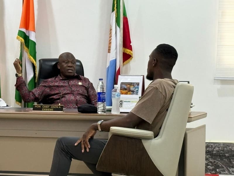 The Chairman gesturing as he speaks from behind his desk while Pr. Joseph Ante listens from an armchair