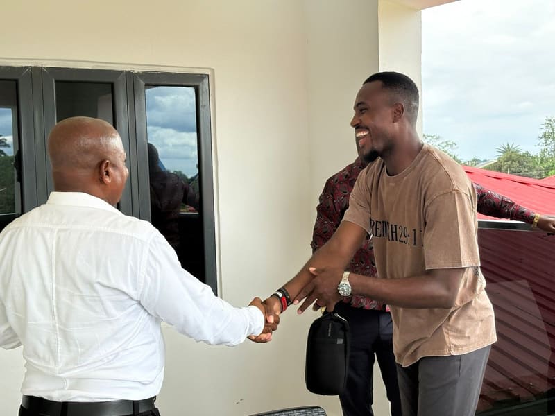 Pr. Joseph Ante shaking hands with a man in a white shirt at a building entrance