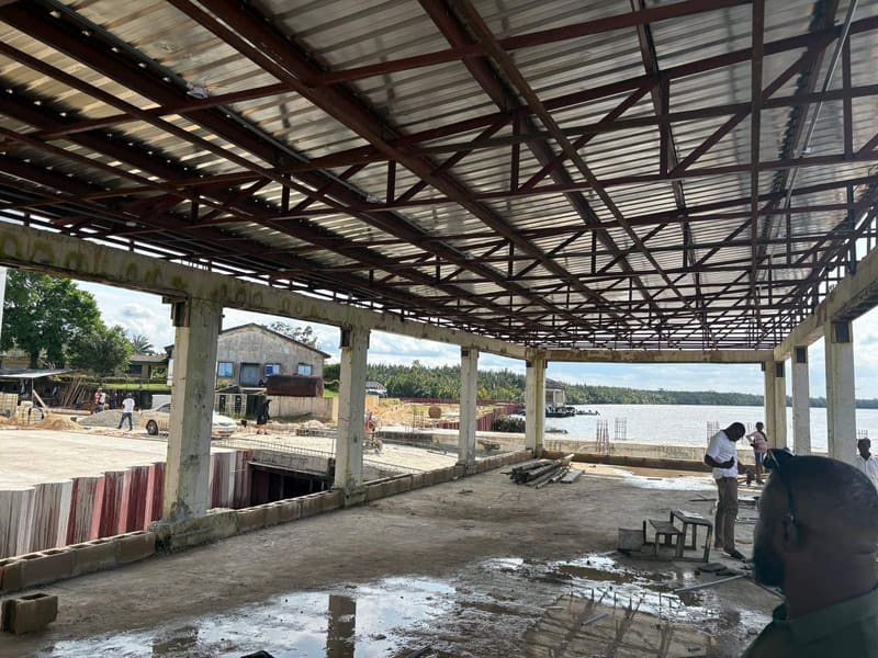 Steel roof frame and concrete columns of a waterfront building under construction, with the river in the distance