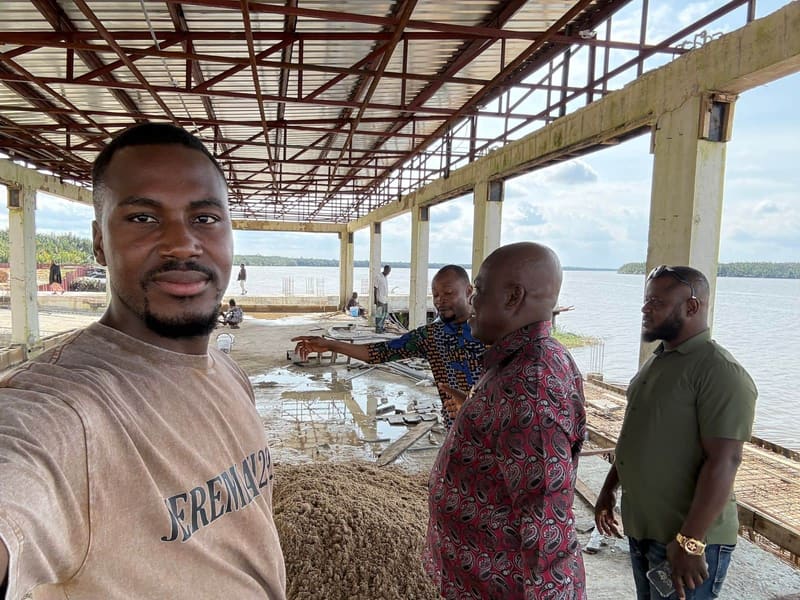 Pr. Joseph Ante takes a photo on the construction site as the Chairman points out the work to two men beneath the steel roof